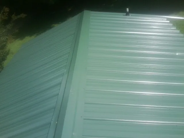 New green metal panels meeting at the ridge of a roof — Flat Roof Repair work by our crew in Noatak