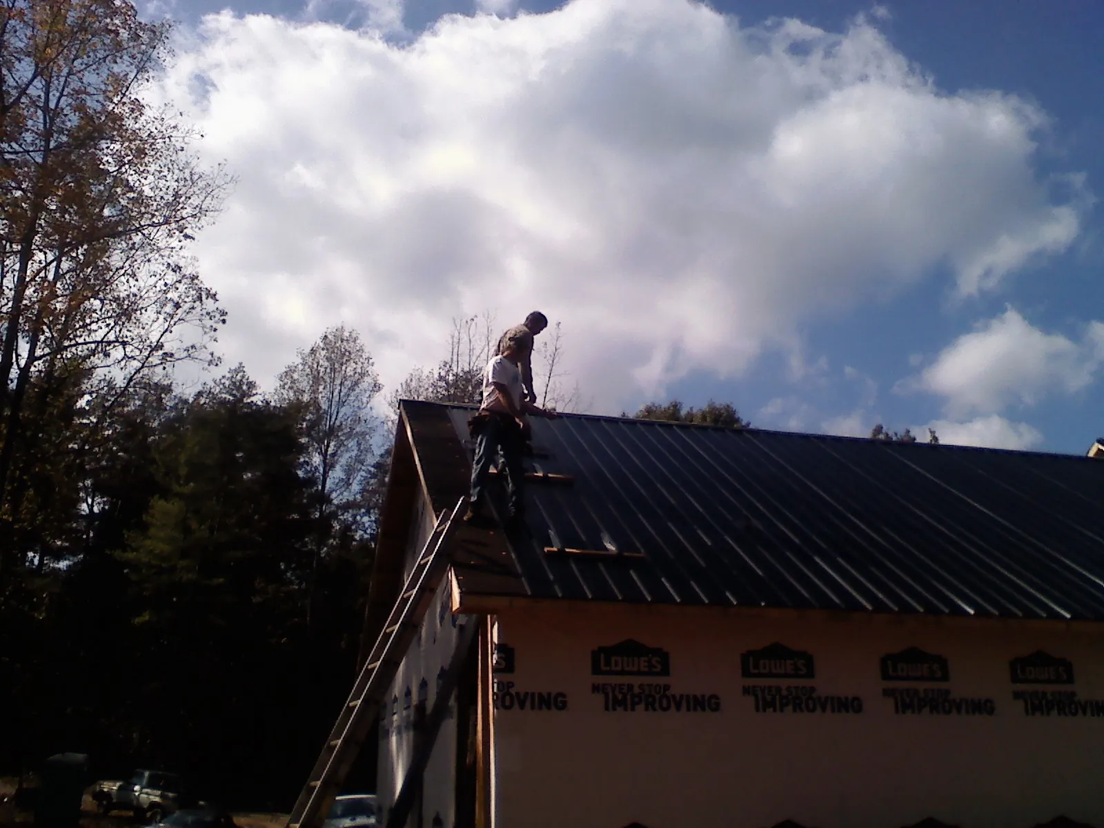 Roofer fastening dark metal panels high against a cloudy sky, from a Roof Inspection job in Noatak
