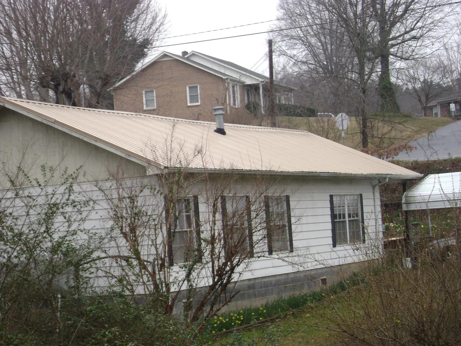Tan metal roof on a white sided house set into a hillside — Commercial Roofing by Roofing Brothers in Noatak
