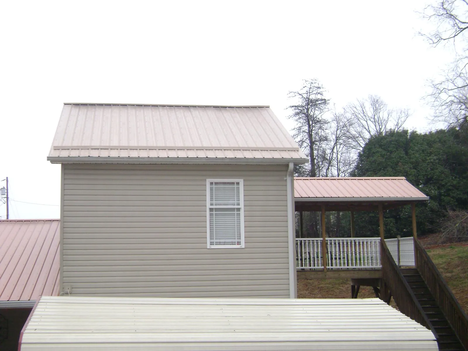 Tan metal roofs on a two story addition and attached porch, from a Roof Replacement job in Noatak